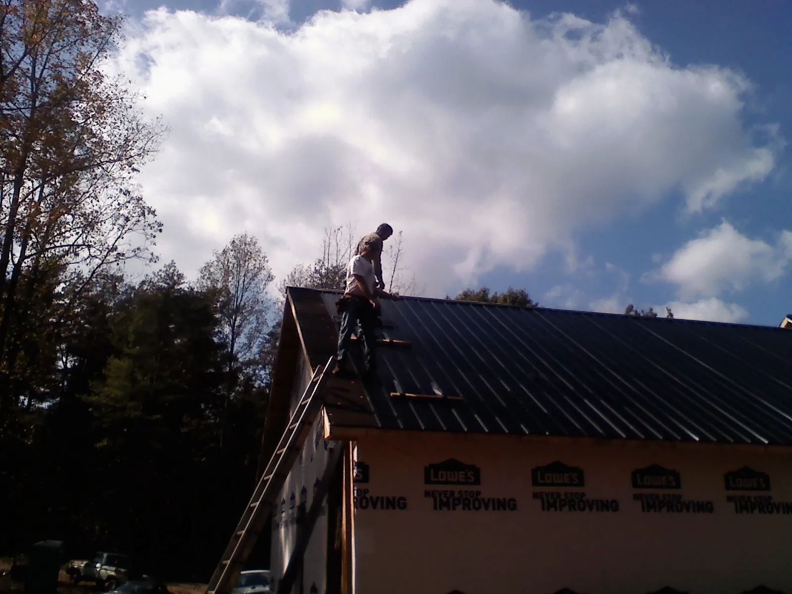 Roofer fastening dark metal panels high against a cloudy sky, from a Roof Inspection job in Etna