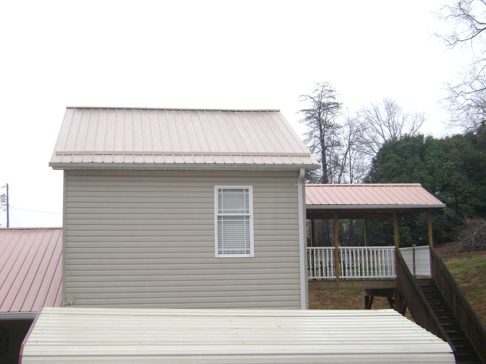 Tan metal roofs on a two story addition and attached porch, from a Roof Replacement job in Etna